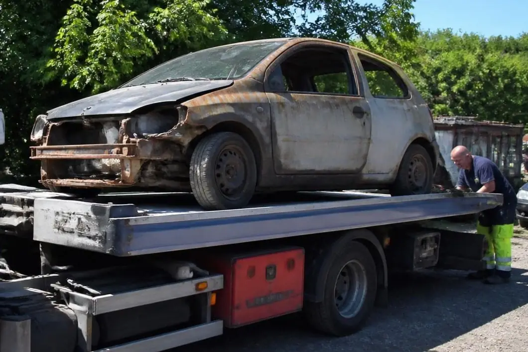 Épave de citadine rouillée posée sur le plateau d’un camion, un homme vérifiant l’arrimage